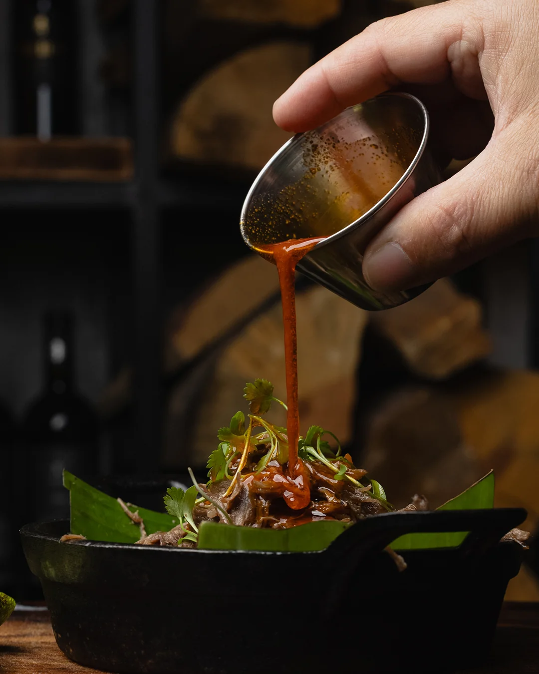 Red salsa being poured over a skillet of tortilla chips and avocado at Origen Gilbert